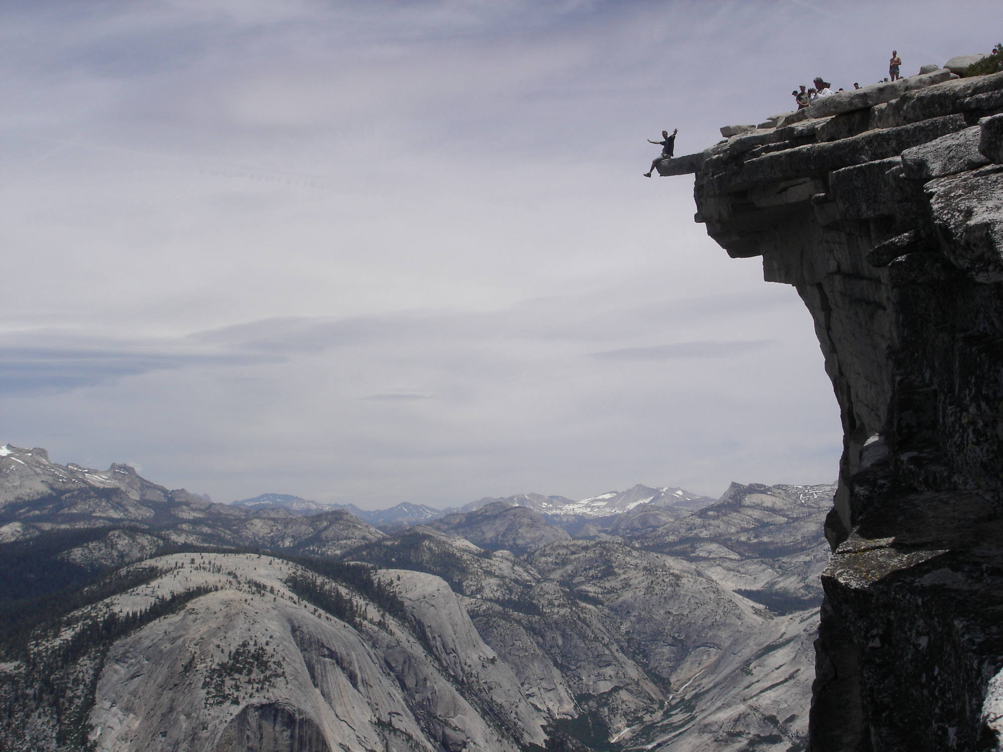 A hiker perched on a granite overhang, legs dangling over the drop.